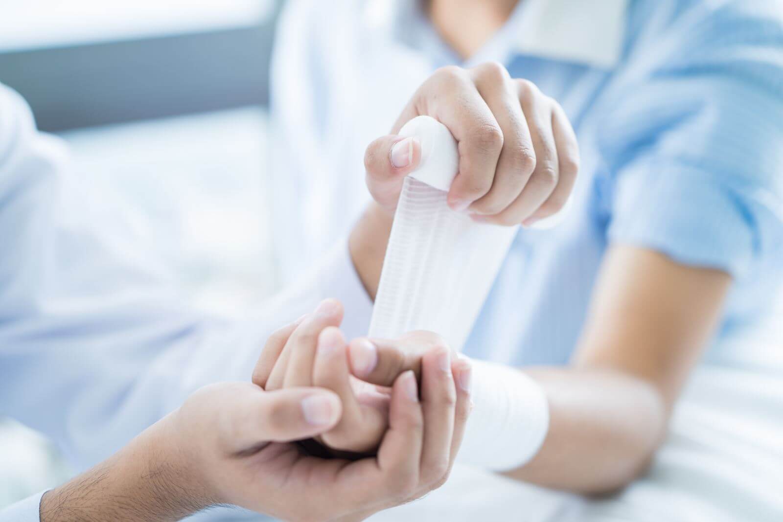 Close up of medical staff wrapping gauze around a patients forearm and hand.