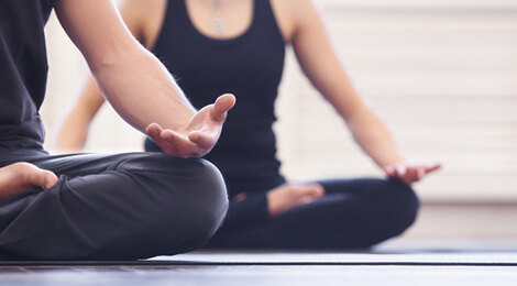 Couple practicing yoga in comfortable seated with hands in meditation resting on knees.