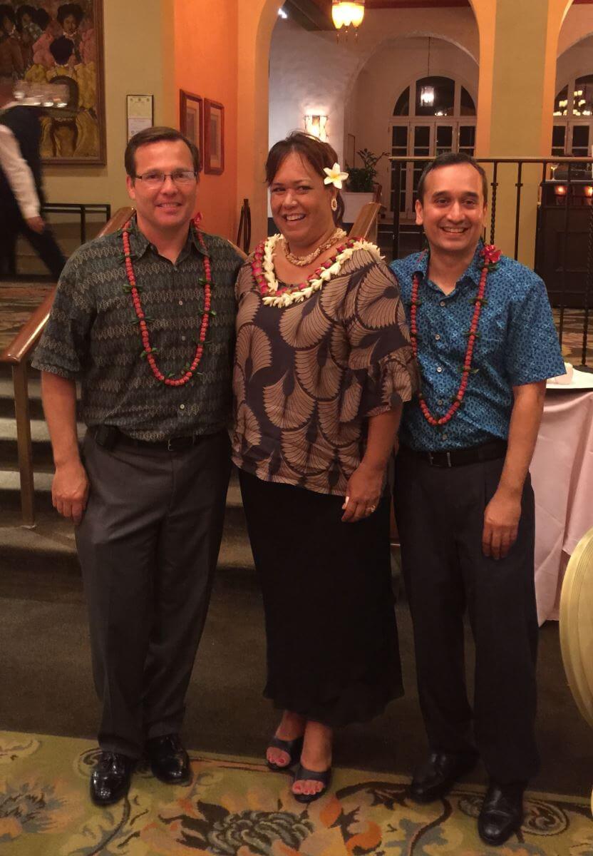3 donors with leis standing together smiling in banquet room.