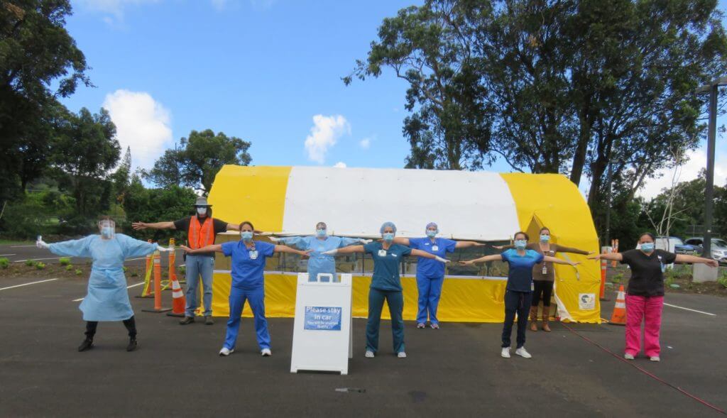 9 medical staff standing arms lengths apart in front of testing tent.