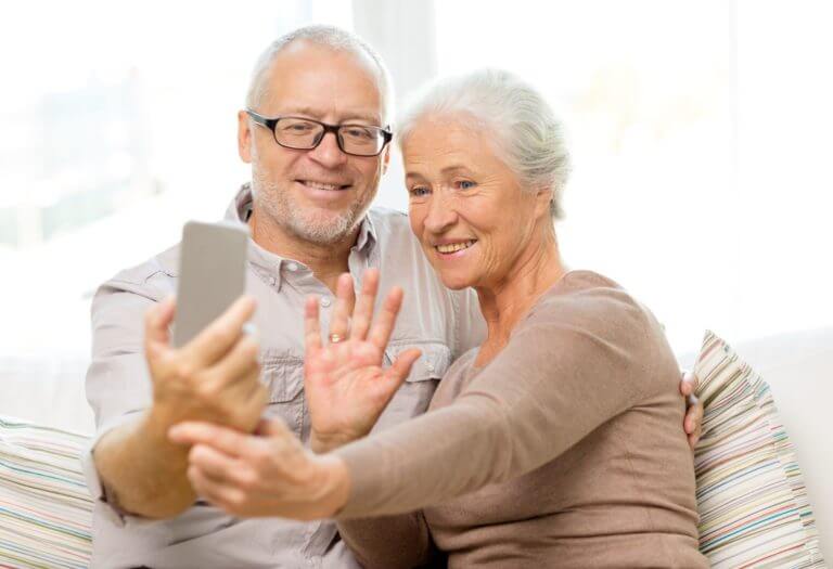 Older male and female couple holding up phone and waving during a video chat