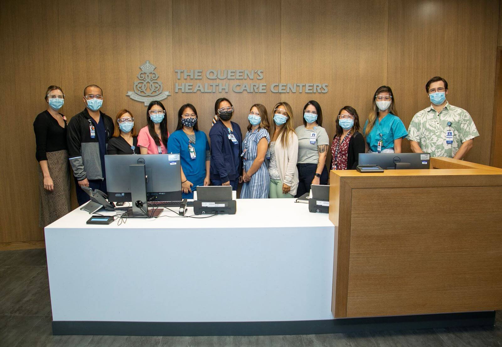 Masked QHS staff stand behind a large desk with the QHS logo on the behind on the wall.
