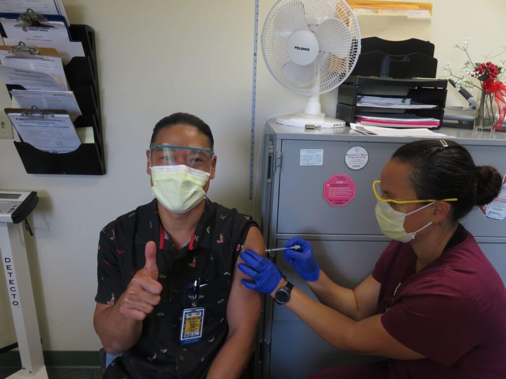 Nurse administering COVID-19 Vaccine to man giving a thumbs up.