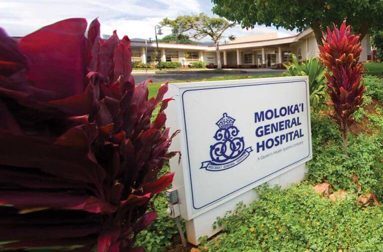 The Molokai General Hospital entrance sign flanked by red plants.