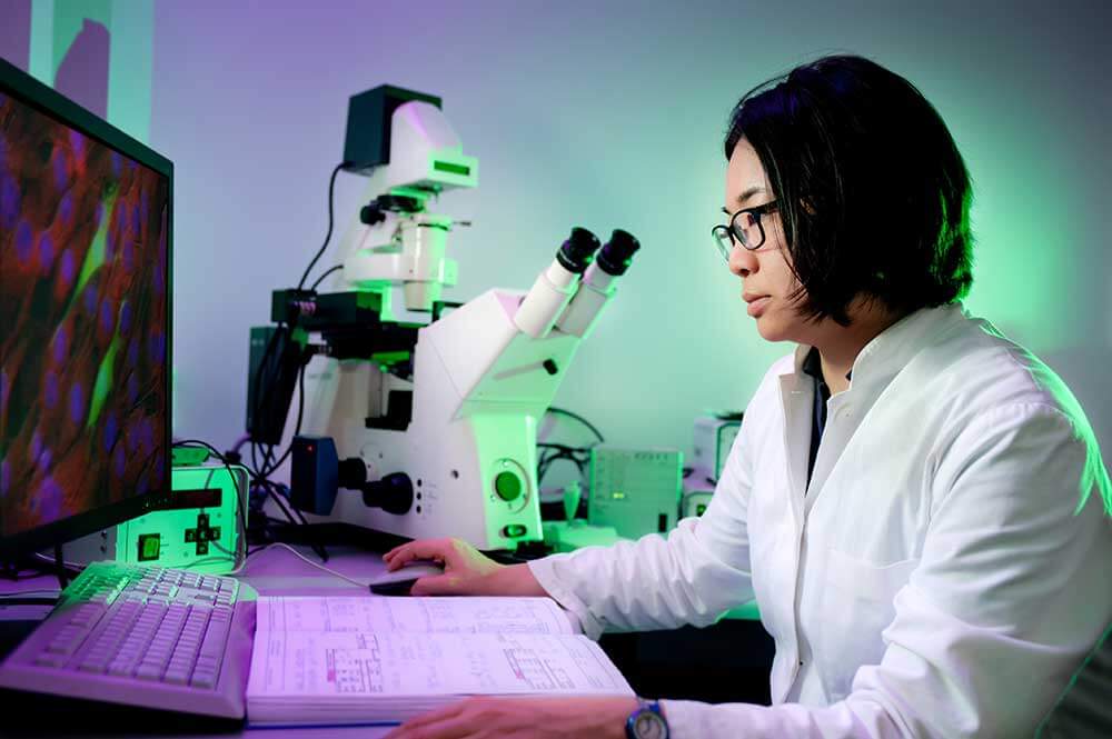 Pathologist looks at microscope images with a large book in front of her