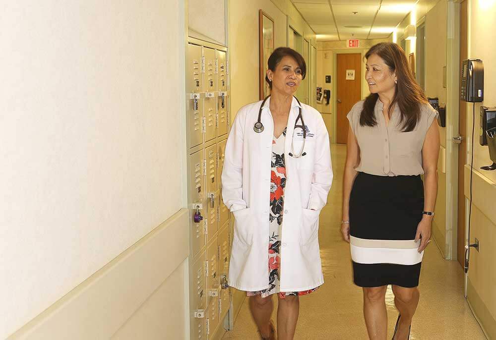 2 female doctors in dresses walk down a hallway