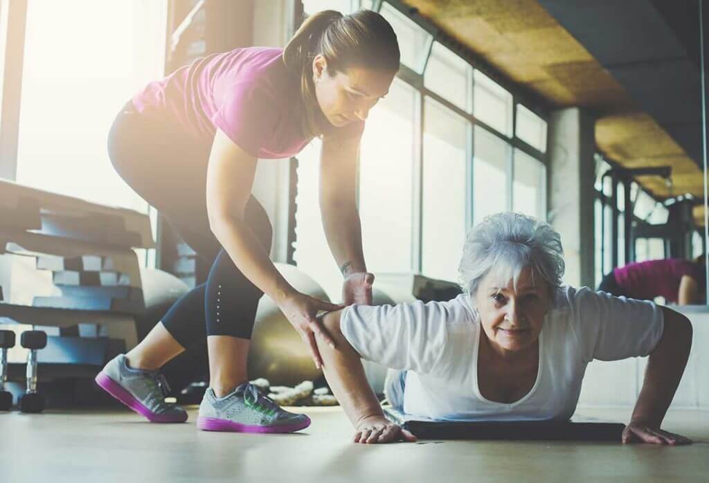 Elderly woman doing a push up with physical therapists helping.