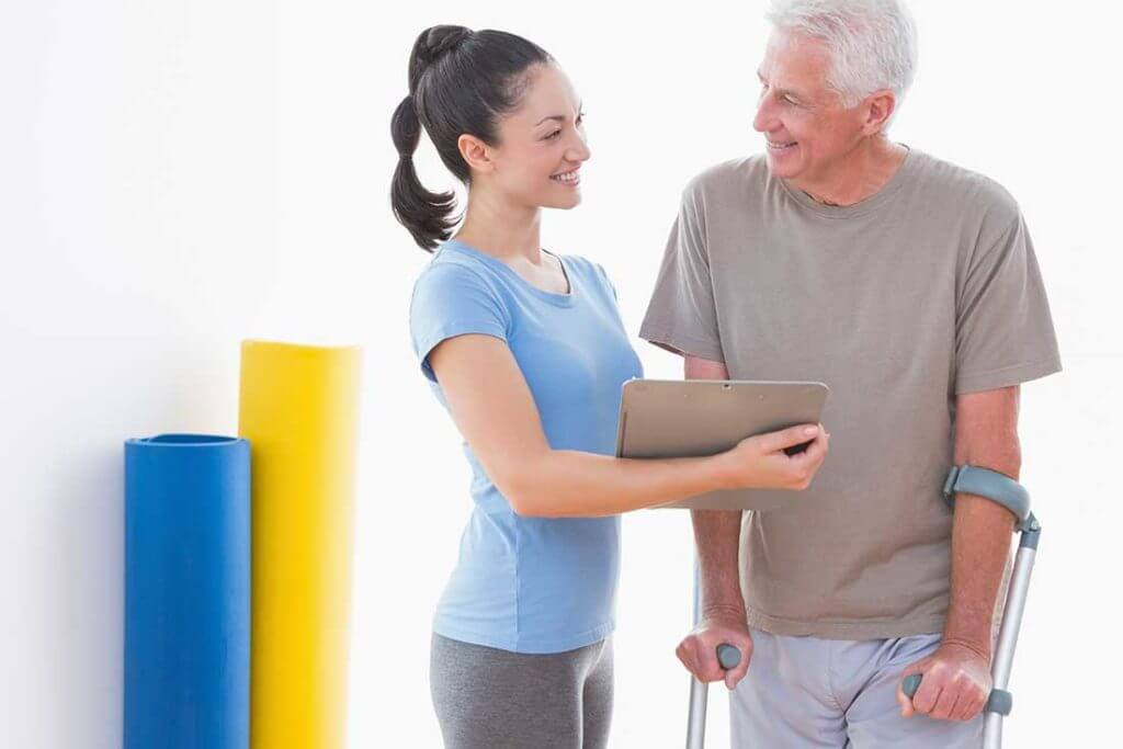 Physical therapists speaking with man using crutches.