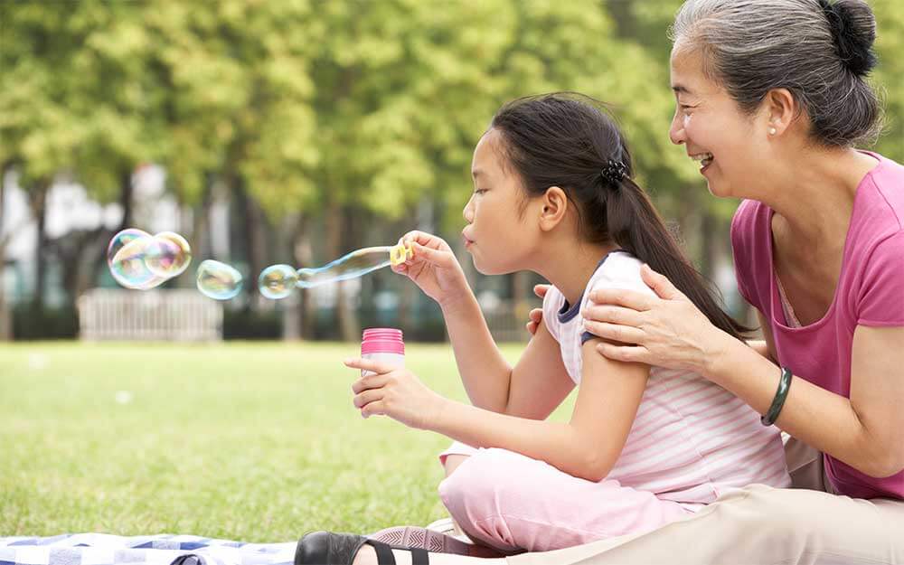 Girl blowing bubbles with Grandmother sitting behind her laughing
