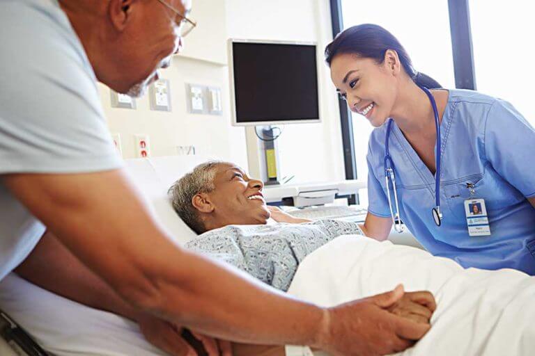 Nurse checking on a woman in hospital with her husband by her side.