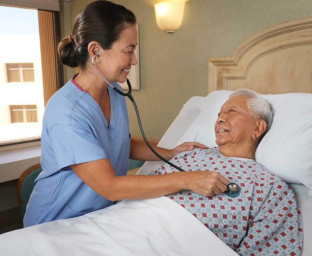 Female nurse using stethoscope on hospitalized patient