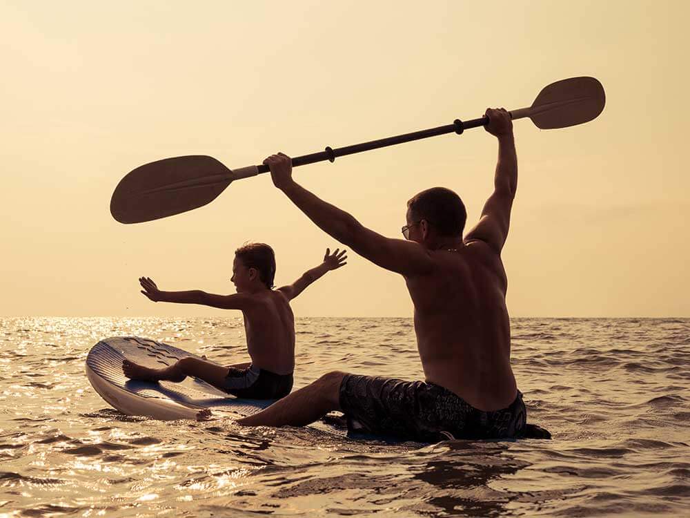 Father and sun sitting paddle boarding