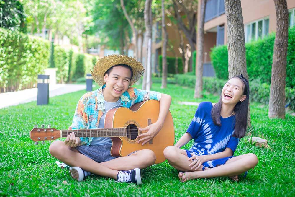 Two kids sit on lawn and play guitar.
