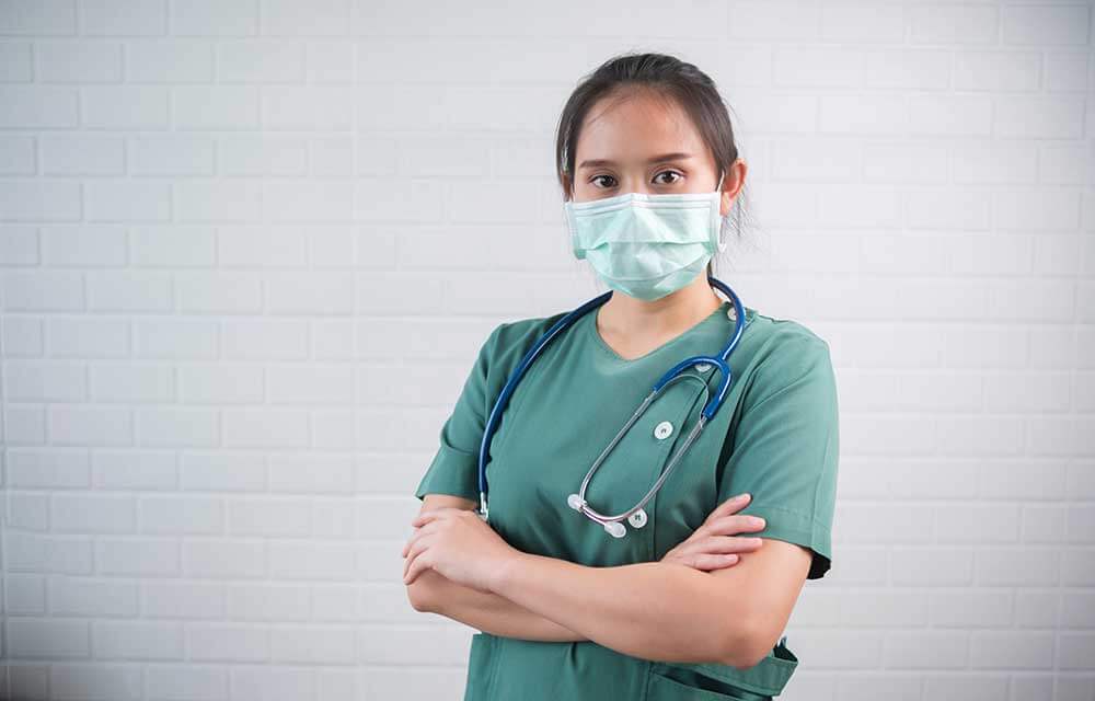 Female nurse with crossed arms and face mask standing in hallway