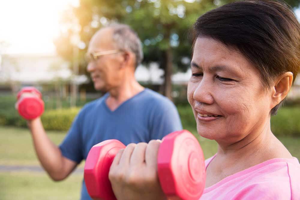 Senior couple lift small weights outside.