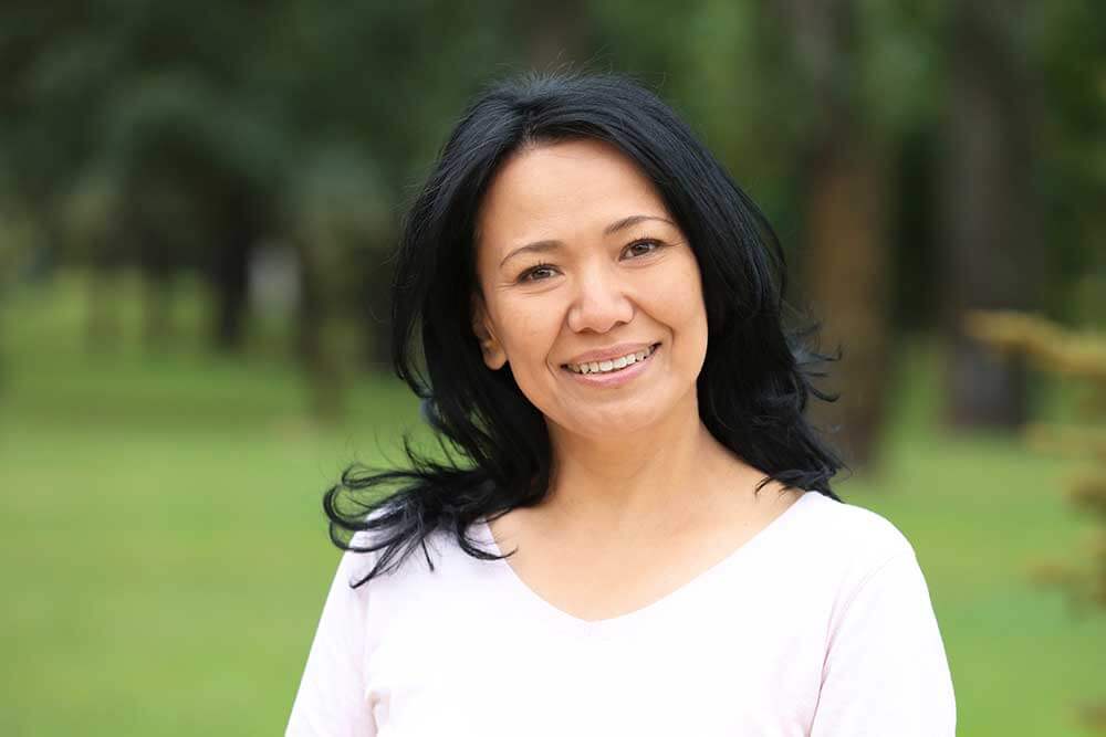 Woman in light pink top smiles with a park in the background.
