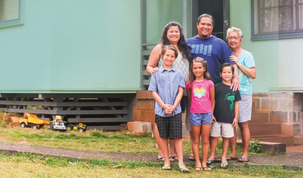 Family of 5 and grandmother standing in front of their home.