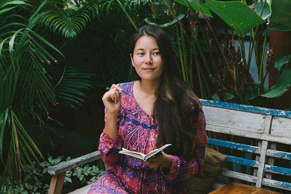Young Woman writing in a journal surrounded by tropical plants.