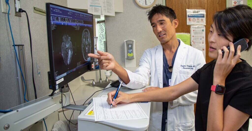 Nuerologists examing head scans of patient and one writes notes on paperwork.
