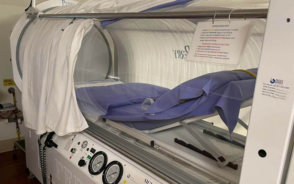 Hyperbolic Oxygen chamber with blue sheets on the bed inside.