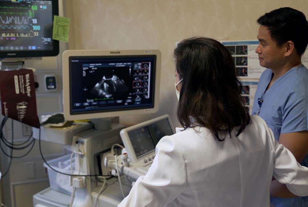 Female cardiologist Dr. Kemble and male nurse looking at ultrasound monitor.