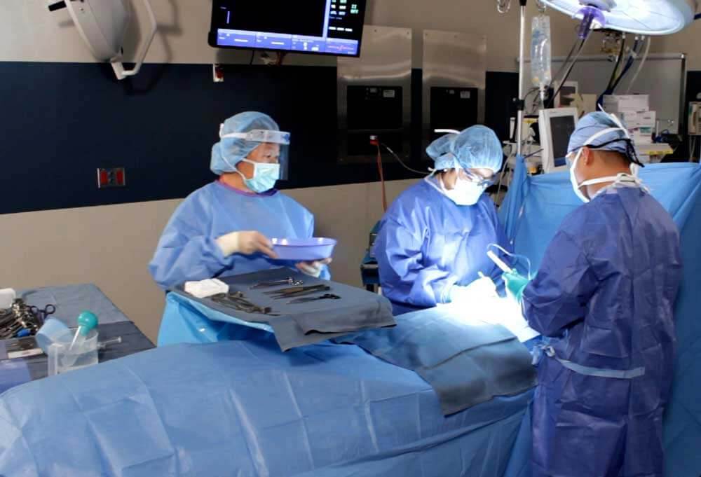 2 surgeons and surgery staff in the OR working on a patient.