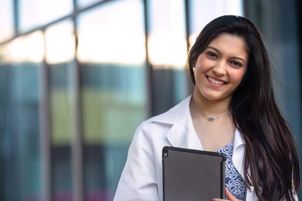 Female intern in a white coat holding tablet.